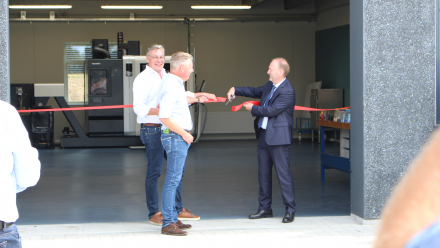 Tre mænd klipper rødt bånd over ind til bygning