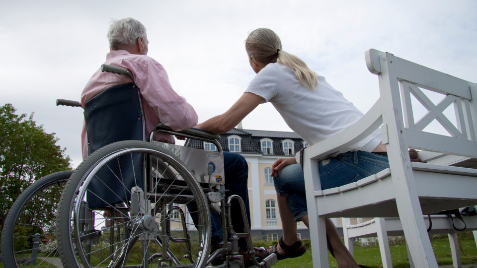 person i kørestol og person ved siden af på bænk